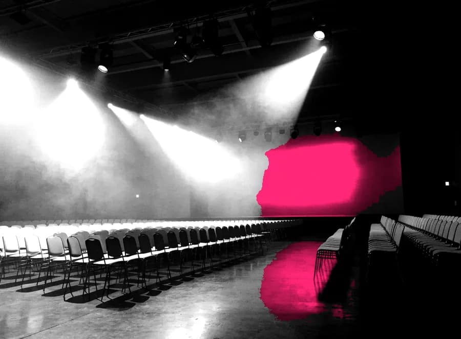 An empty event hall before doors, stacked chairs and a bare stage