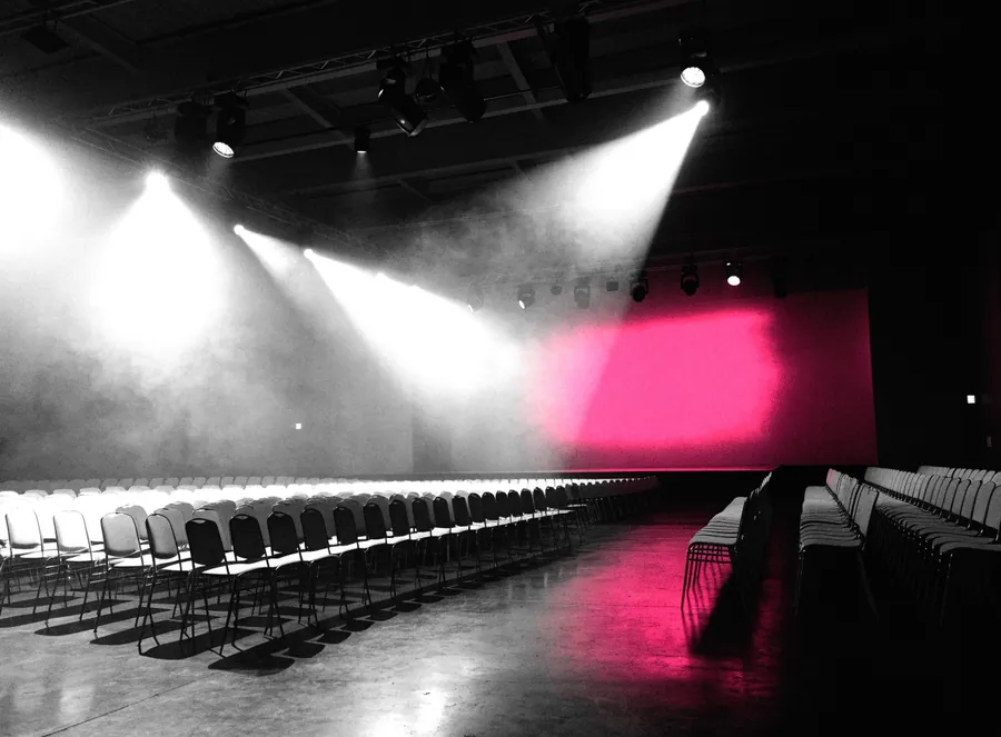 An empty event hall before doors, stacked chairs and a bare stage
